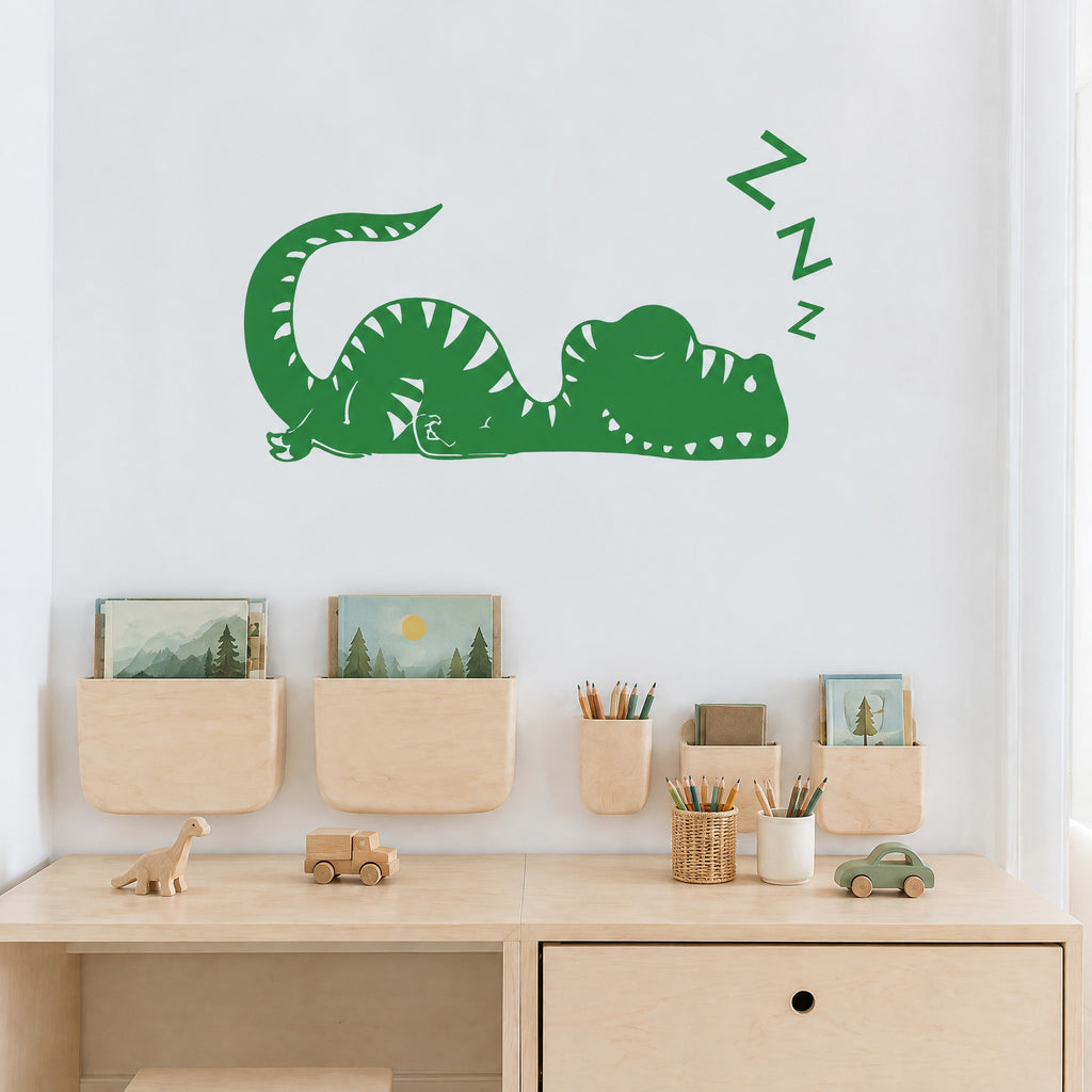 Sticker mural dinosaure endormi vert forêt au-dessus d'un bureau en bois clair de chambre de garçon