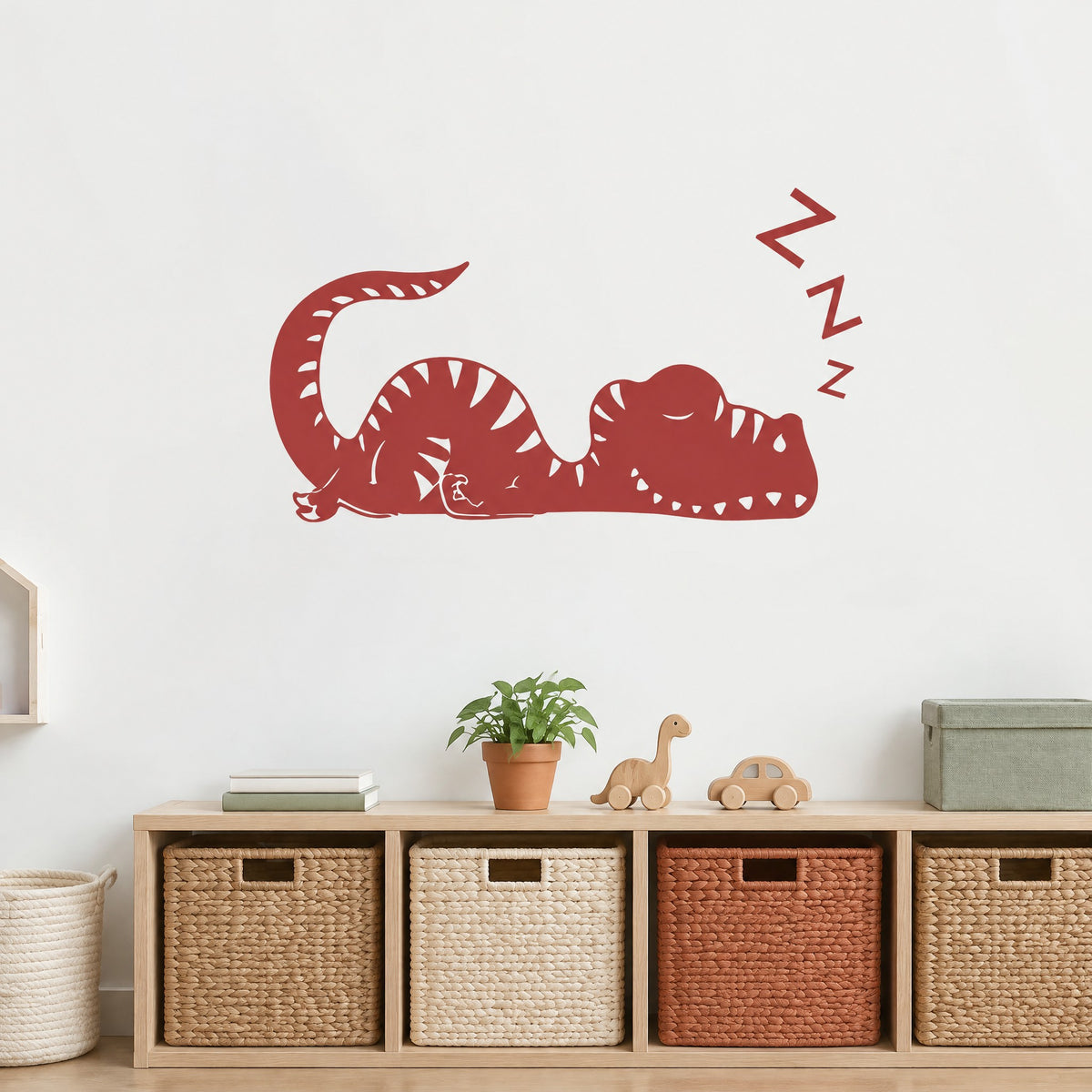 Sticker mural dinosaure endormi rouge brique au-dessus d'un meuble de rangement en chêne et de paniers tressés
