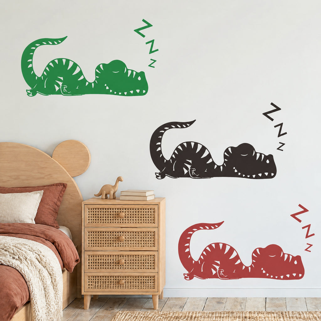Les trois coloris du sticker mural dinosaure endormi, vert forêt, noir et rouge brique, dans une chambre de garçon avec lit en bois et commode cannée