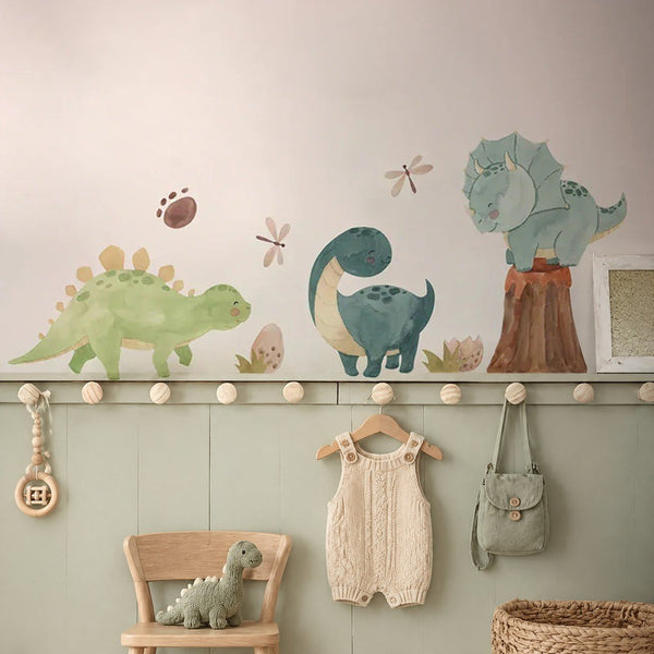 Frise de stickers muraux dinosaures à l'aquarelle au-dessus d'une patère avec une barboteuse en tricot