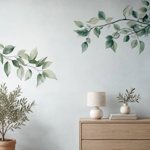 Adesivi murali rami verde pastello sopra una cassettiera in rovere chiaro con lampada in ceramica e olivo