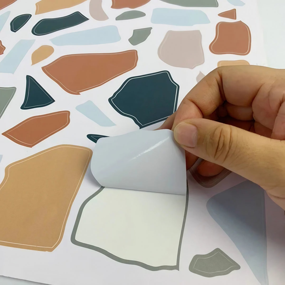 Main qui décolle une forme terrazzo prédécoupée de sa planche