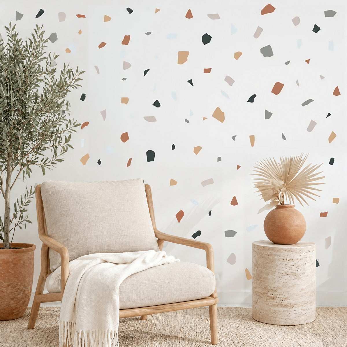 Stickers muraux confettis terrazzo terre cuite dispersés sur un mur blanc de salon, au-dessus d'un fauteuil en chêne et lin, près d'un olivier en pot