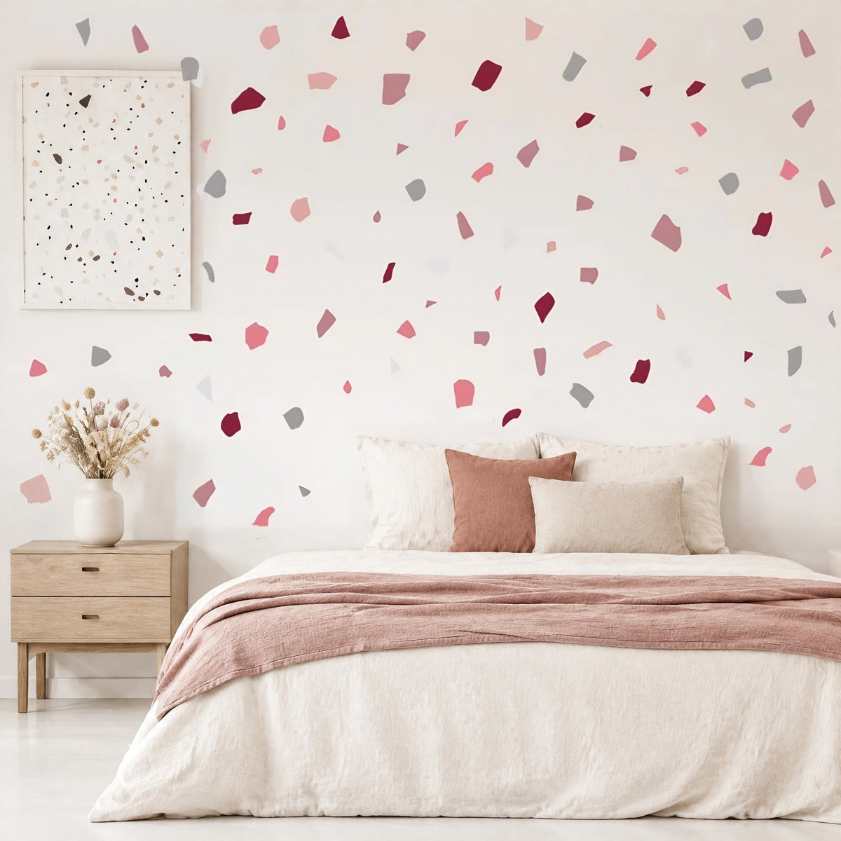 Confettis terrazzo bordeaux, rose et gris au mur, au-dessus d'un lit en linge crème et vieux rose