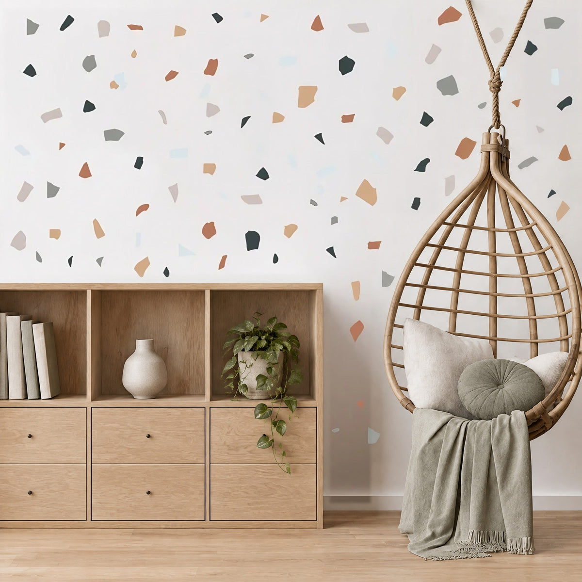 Confettis terrazzo terre cuite au mur d'un coin lecture de chambre, fauteuil suspendu en rotin et meuble en chêne clair