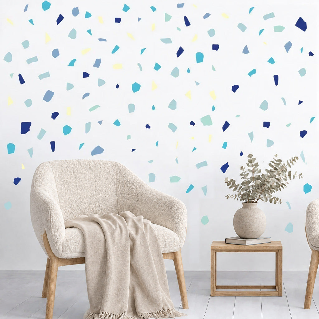 Stickers muraux confettis terrazzo bleus au-dessus d'un fauteuil bouclette crème et d'une table d'appoint en chêne