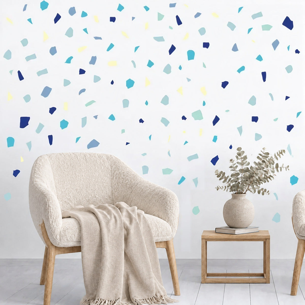 Stickers muraux confettis terrazzo bleus au-dessus d'un fauteuil bouclette crème et d'une table d'appoint en chêne
