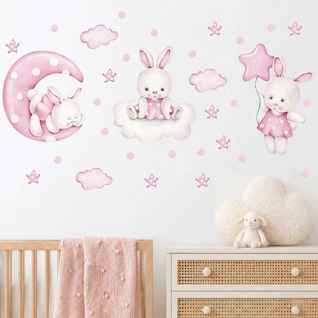 Stickers muraux lapins aquarelle rose sur la lune, sur un nuage et avec un ballon étoile, au-dessus d'un lit bébé en bois clair et d'une commode cannée