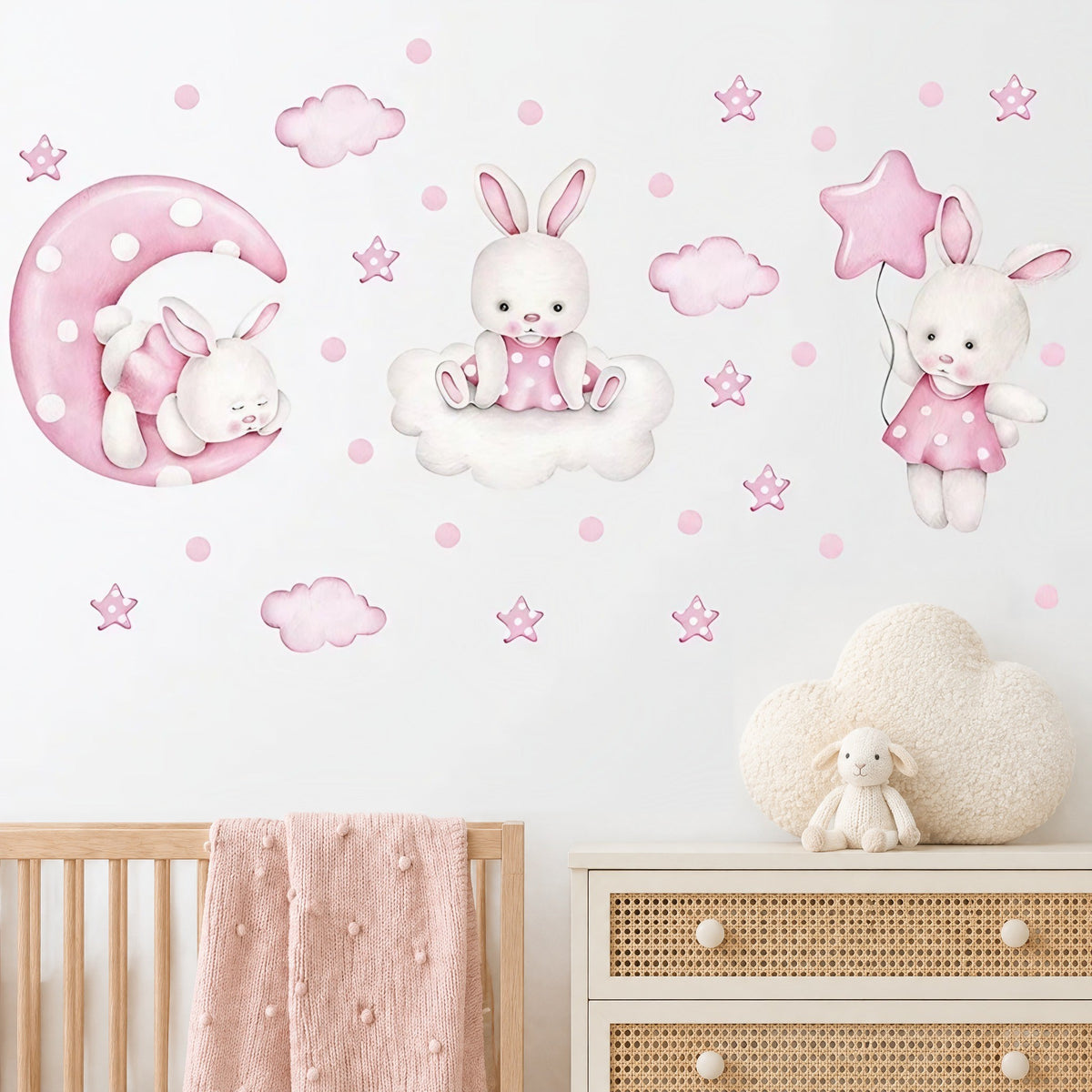 Stickers muraux lapins aquarelle rose sur la lune, sur un nuage et avec un ballon étoile, au-dessus d'un lit bébé en bois clair et d'une commode cannée