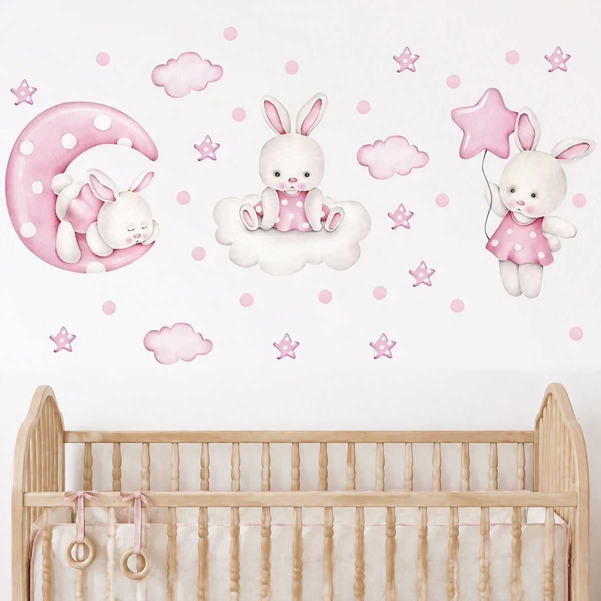 Stickers lapins, lune, nuages et étoiles roses posés au-dessus d'un lit à barreaux en bois naturel