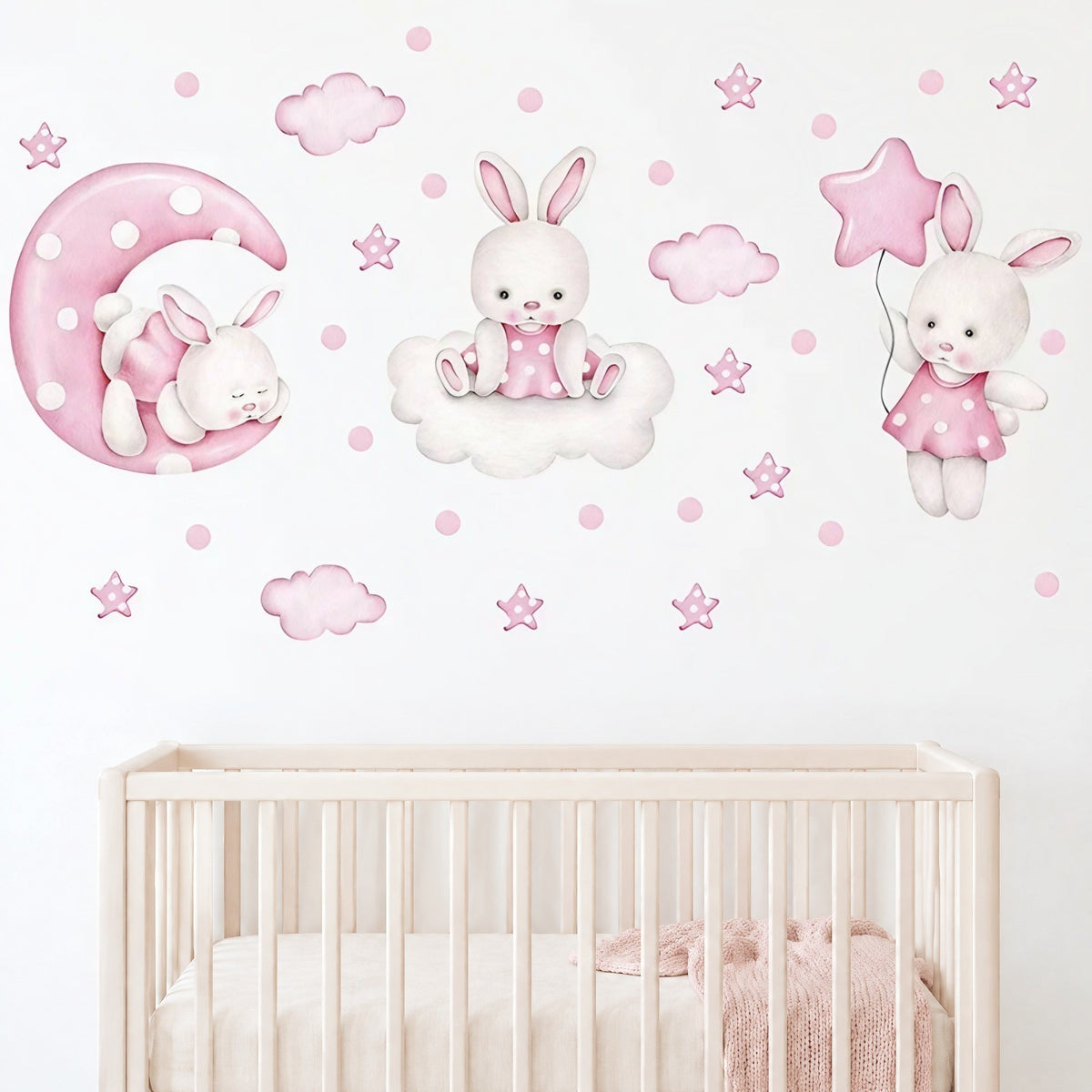 Composition de stickers lapins, lune et étoiles roses au-dessus d'un lit bébé à barreaux crème