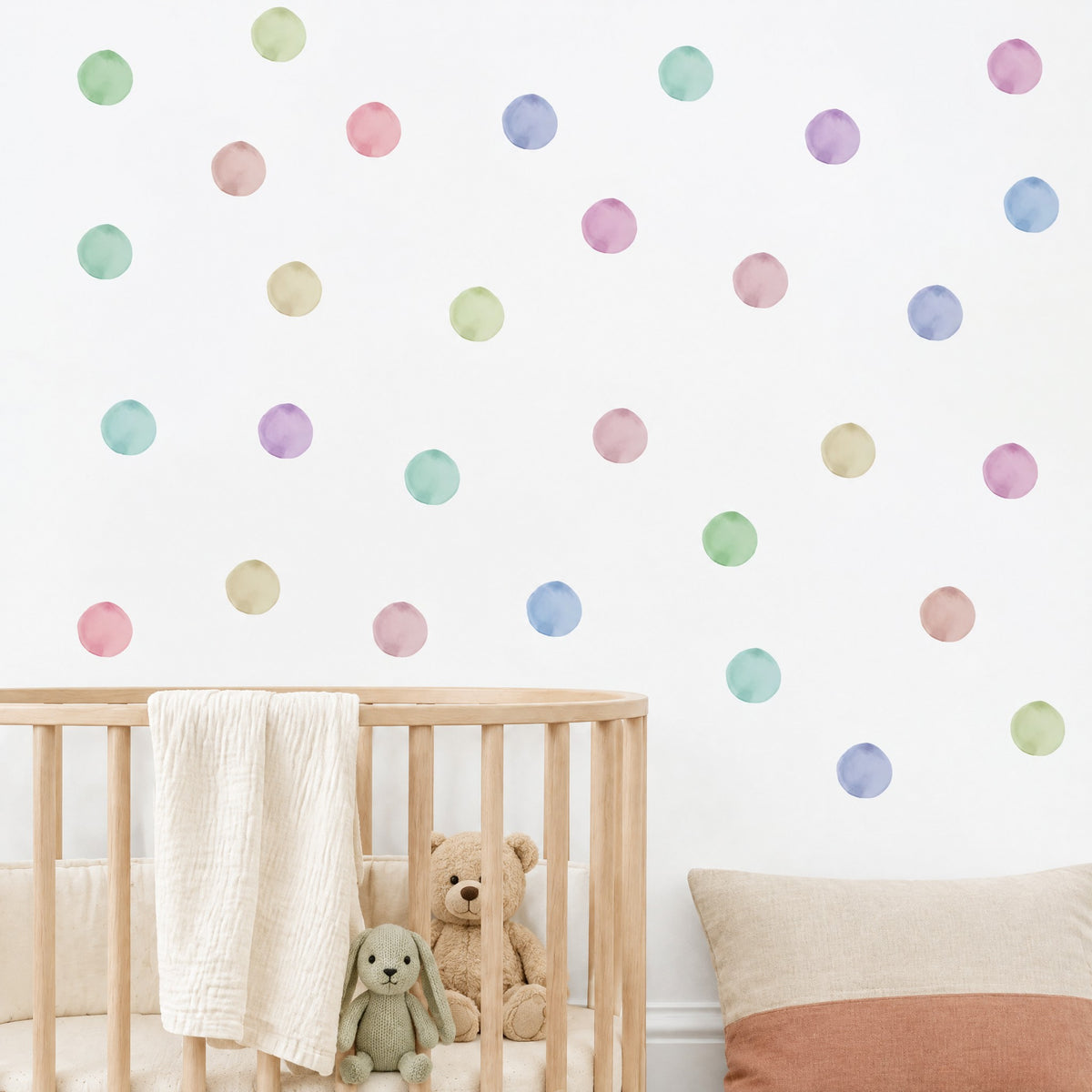 Stickers pois ronds pastel au mur d'une chambre de bébé, au-dessus d'un berceau en bois naturel et de peluches