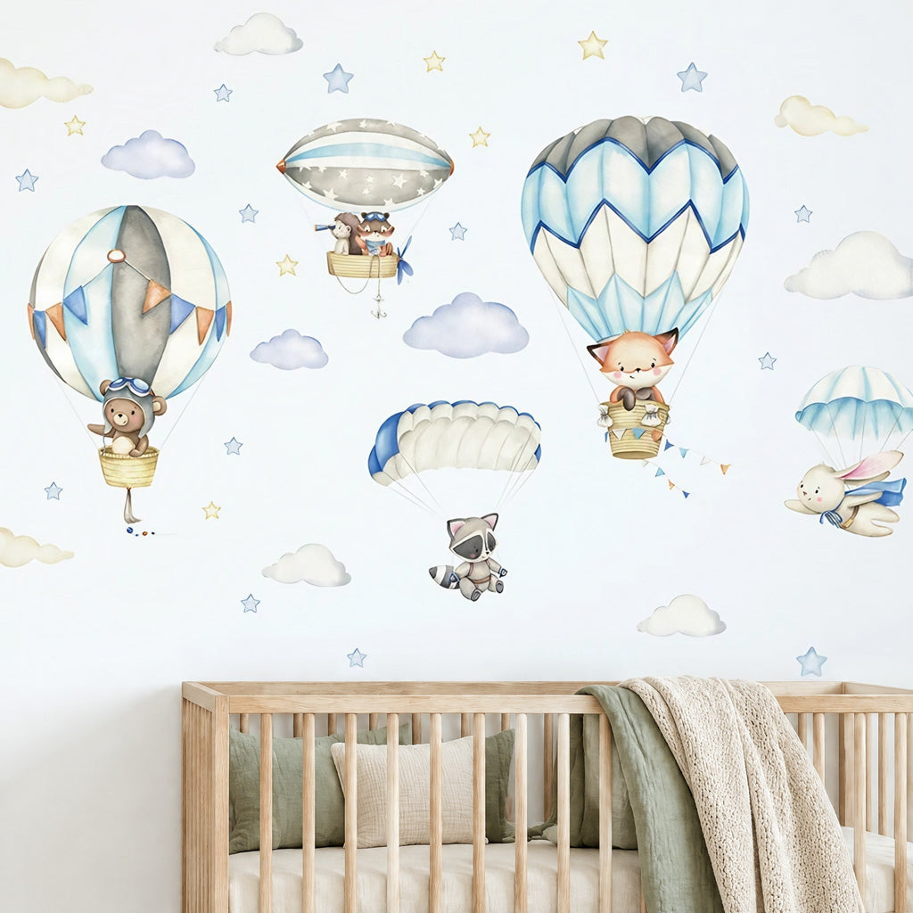 Stickers muraux renard et ourson en montgolfière au-dessus d'un lit bébé en bois clair, lapin et raton laveur en parachute