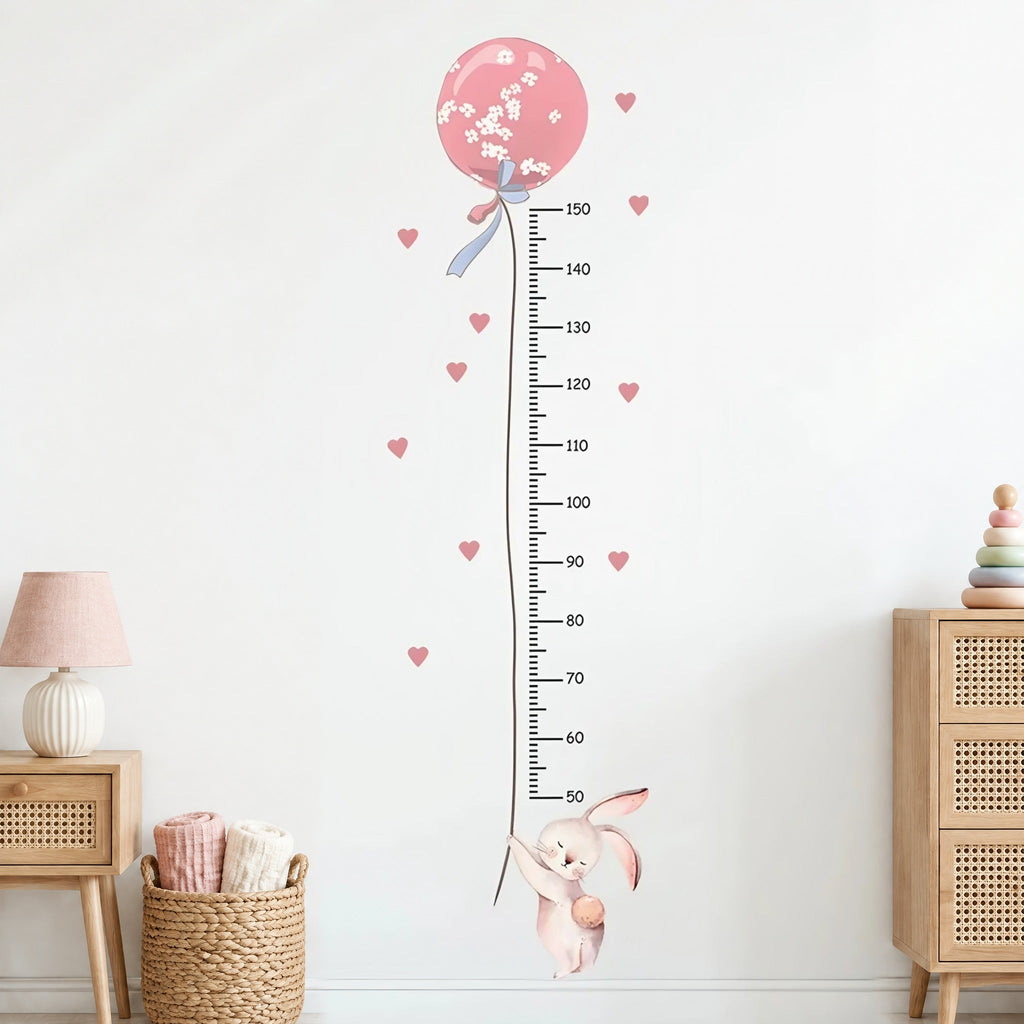 Stickers muraux toise lapin et ballon rose à fleurs blanches, règle graduée de 50 à 150 cm et cœurs roses, entre une table de chevet et une commode cannées en chêne