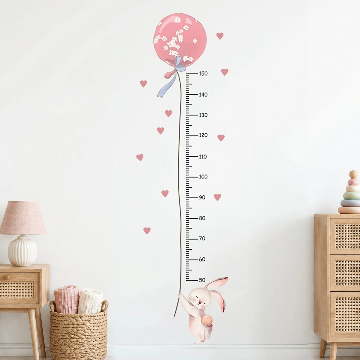 Stickers muraux toise lapin et ballon rose à fleurs blanches, règle graduée de 50 à 150 cm et cœurs roses, entre une table de chevet et une commode cannées en chêne