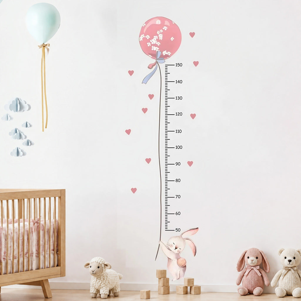 Toise murale lapin accroché à un ballon rose près d'un lit bébé à barreaux en bois clair et de peluches tricotées